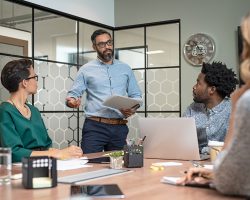 Confident mature businessman giving a presentation to his team in office. Business brief with annual goals with employees and mature boss in meeting room. Multiethnic leader training business people.