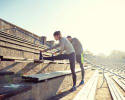 fitness, sport, exercising and lifestyle concept - couple stretching leg on stands of stadium