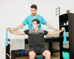 Physical therapist helping male patient using resistance band to exercise in hospital