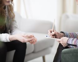 Cropped photo of a therapist writing down notes during therapy with her female patient